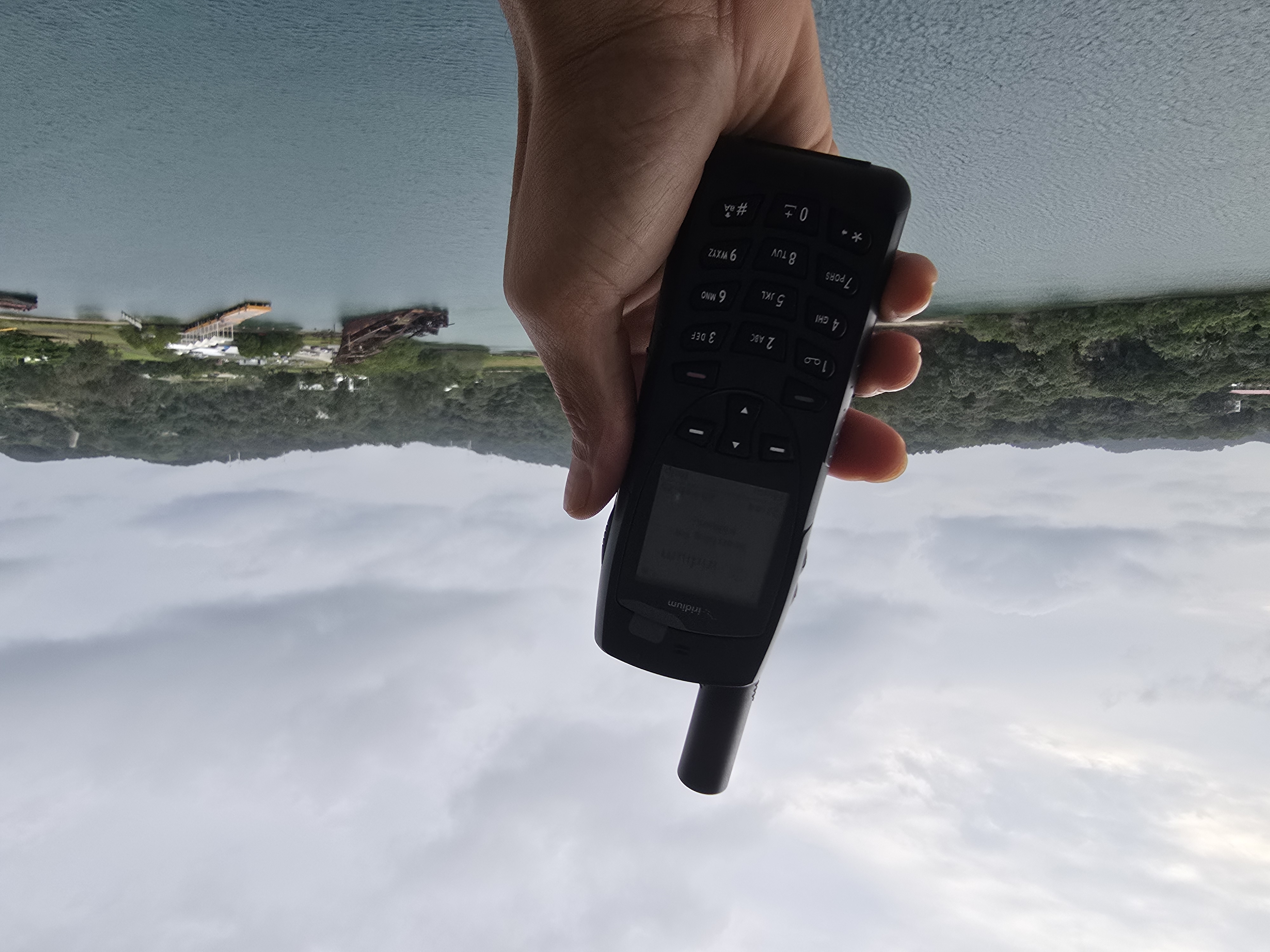 Hand holding satellite phone for maritime communications with waterfront background